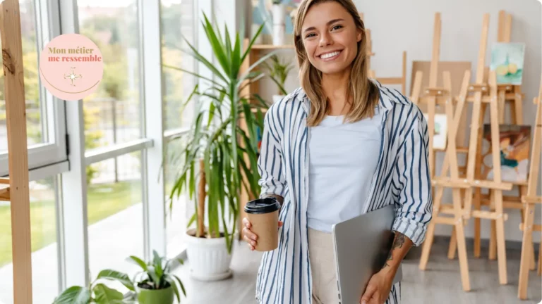 Femme souriante tenant un café et un ordinateur portable dans un atelier lumineux, illustre la personne qui a trouvé un métier en accord avec sa personnalité